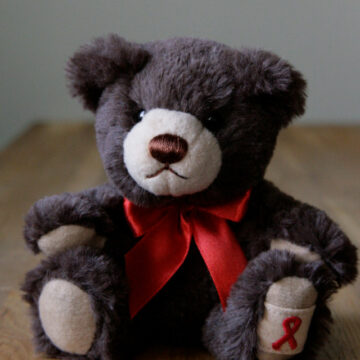 Bild eines Teddybären mit einer roten Aidshilfeschleife um den Hals.