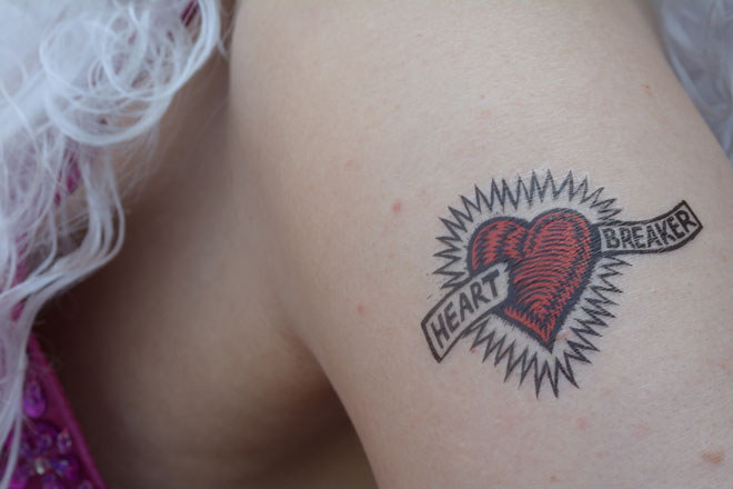 Photo eines Tattos in Form des Heartbreaker Logos: Ein Herz mit Strahlenkranz und Textfähnchen (Hertbreaker)